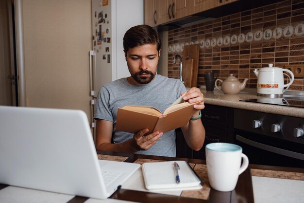 魅力的な若い流行に敏感な男は、ホーム オフィスで本を読んで焦点を当ててください。