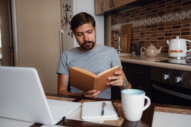 魅力的な若い流行に敏感な男は、ホーム オフィスで本を読んで焦点を当ててください。