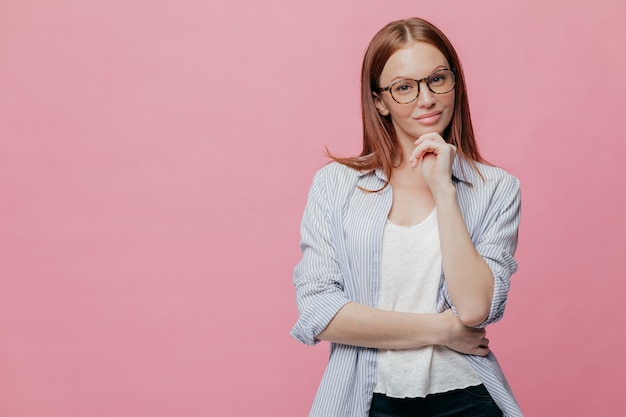 Attraente giovane donna tiene le mani parzialmente incrociate, guarda seriamente la fotocamera