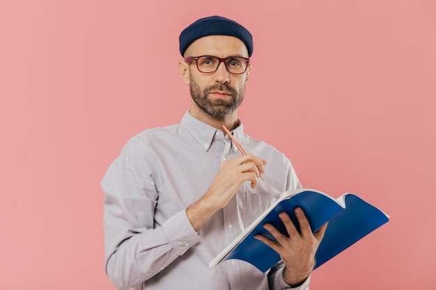 Il giovane maschio attraente tiene il libro di testo, prende le note nell'organizzatore, vestito formalmente.