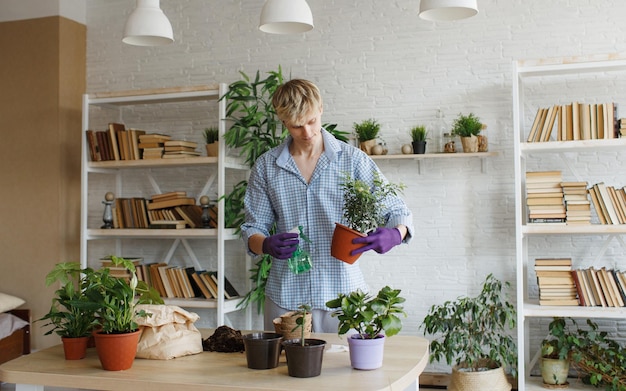 国内の植物を世話する魅力的な若い男が花を移植し、植木鉢に地球を注ぎます