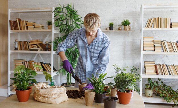 国内の植物を世話する魅力的な若い男が花を移植し、植木鉢に地球を注ぎます