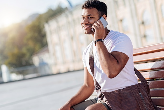 Attractive young man expressing positivity and sitting on the bench while looking forward