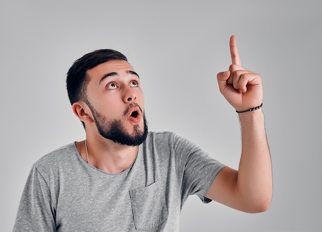 Attractive young man in gray t-shirt pointing up with his finger isolated on gray background