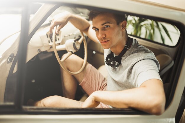 An attractive young man is sitting in a vintage car.