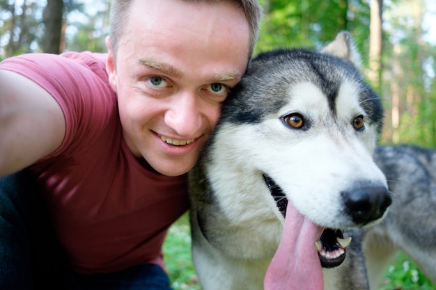 Il giovane attraente fa il selfie con il suo malamute del cane su una passeggiata nella foresta