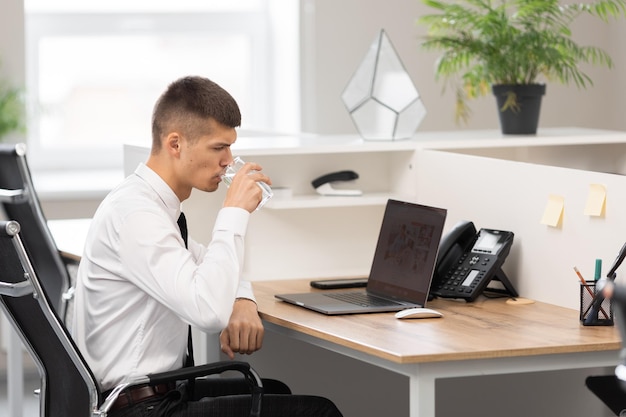 Attractive young man in the office at work holding a glass of water in his hand focus on details