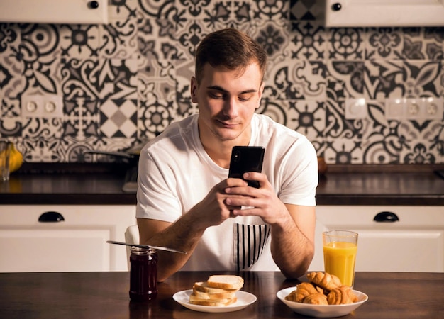 Attractive young man in pajama texting on his smartphone while
having breakfast at home