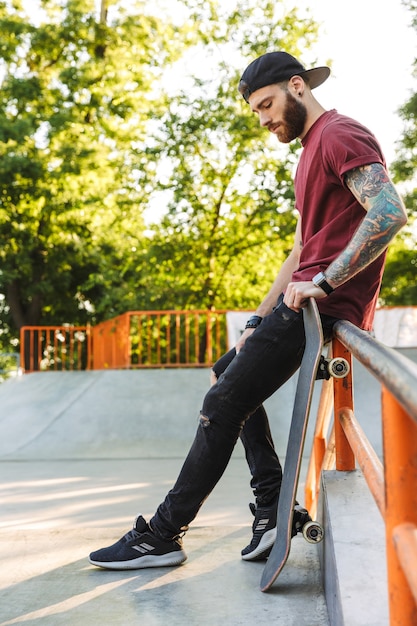 Attractive young man sitting at the skate park ramp with a skateboard