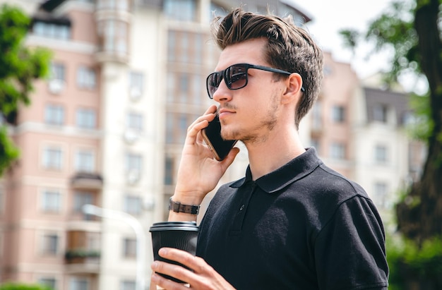 Привлекательный молодой человек в солнечных очках разговаривает по смартфону в городе