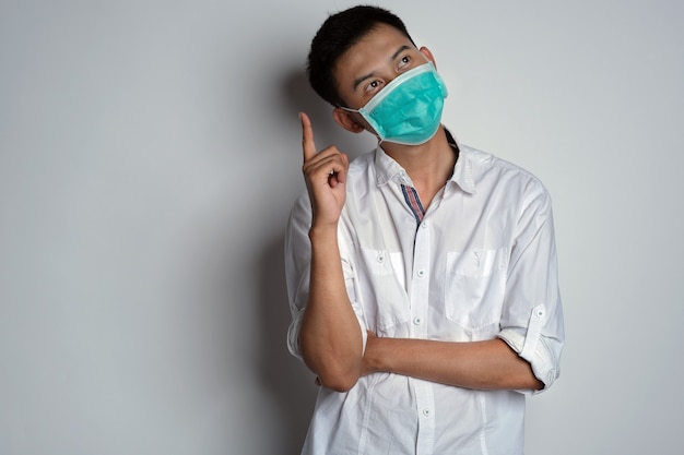 Foto giovane attraente che indossa una maschera per la salute con una posa di espressione pensante e la mano rivolta verso l'alto