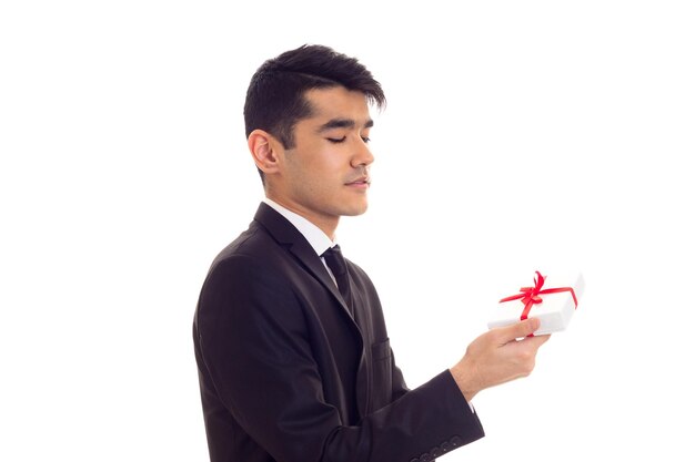 Attractive young man with black hair in white shirt and black suit with tie holding a present on white background