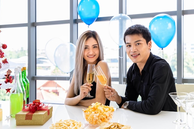 Attractive young man and woman celebrate Christmas and New Year in office party clinking champagne glass with snack and beverage on table