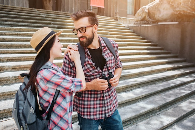 Attractive young man and woman stand on stairs and look at each other. She holds hands on his shoulders. They smile to each other. People look lovely.