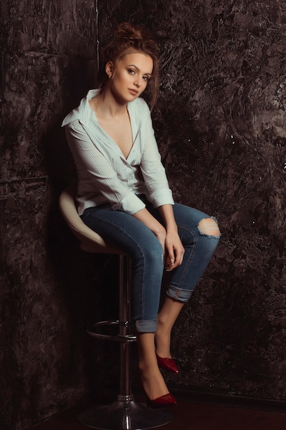 Attractive young model sitting on a chair  in striped and torn jeans