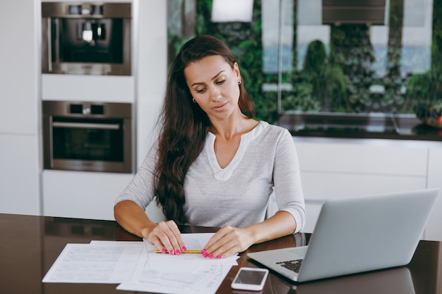 The attractive young modern business woman working with documents and laptop in the kitchen at home