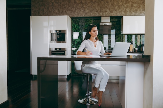 The attractive young modern business woman working with documents and laptop in the kitchen at home