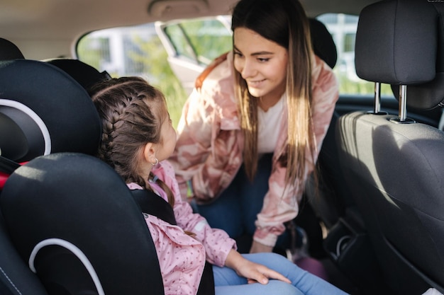 Attractive young mother put her daughter in a car seat and fastens her seat beltsProtection during the trip in the car