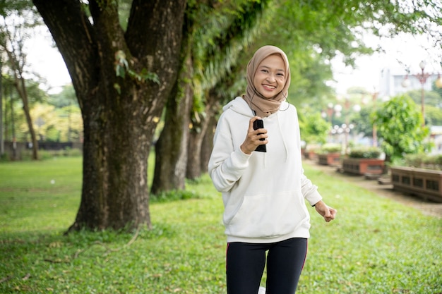 屋外で実行している魅力的な若いイスラム教徒の女性。ジョギング幸せなアジアのスポーツの女の子の笑顔