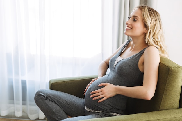 Attractive young pregnant blonde woman sitting in an armchair at home