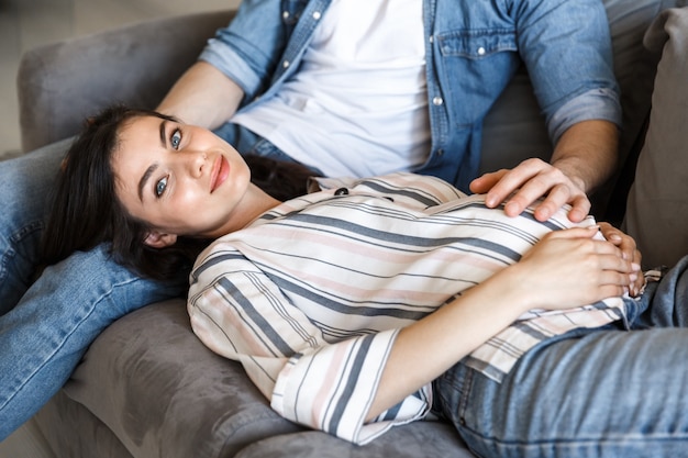 Attractive young pregnant couple relaxing on a couch at home, hugging