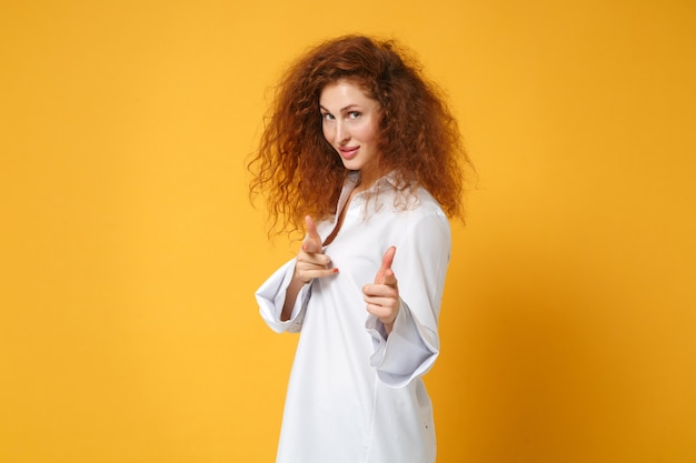 Attractive young redhead woman girl in casual white shirt posing isolated on yellow orange wall