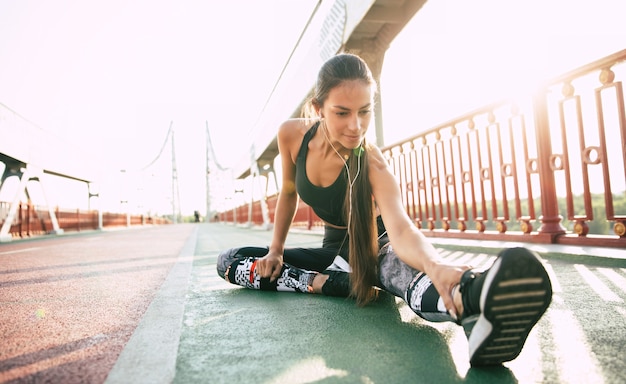 Attractive young slim woman in sport wear is warm up and stretching on the bridge