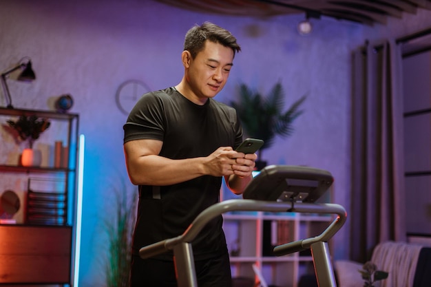 Attractive young sports asian man using phone looking online\
fitness class while working out