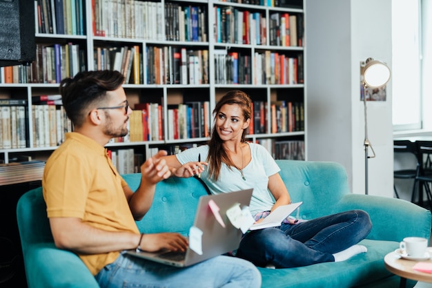 Attractive young students man and woman sitting in university library and learning.