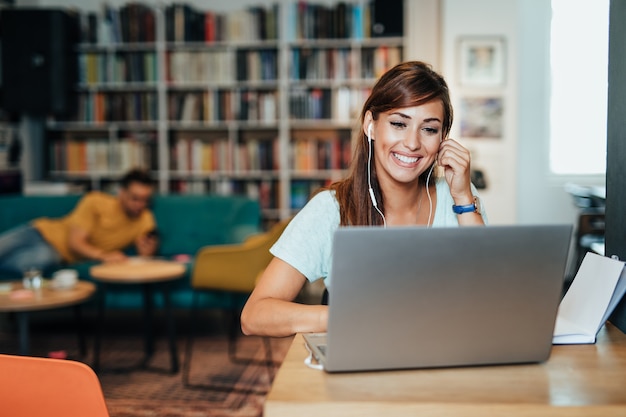 Giovani studenti attraenti seduti in una biblioteca scolastica e che usano il computer portatile per imparare e scrivere.