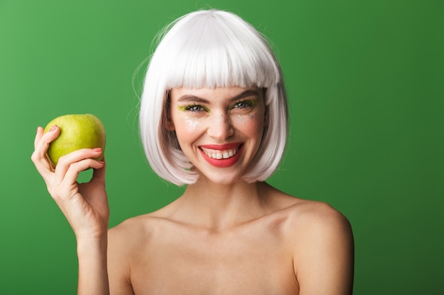 Attractive young topless woman wearing short white hair standing isolated, eating an apple