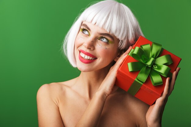 Attractive young topless woman wearing short white hair standing isolated, holding red gift box