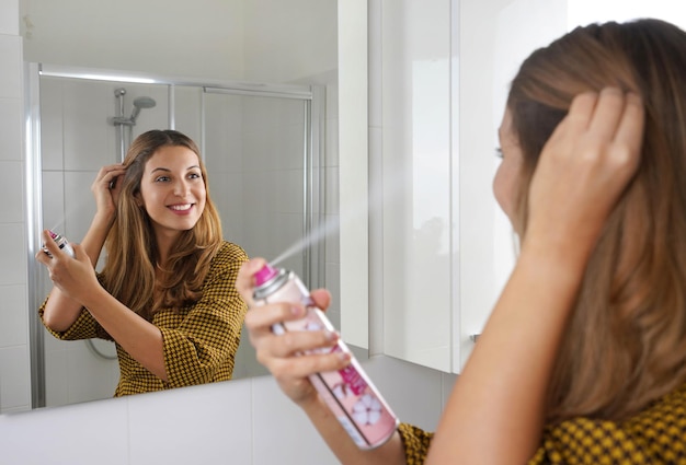 Attractive young woman applying dry shampoo on her hair. Fast and easy way to keep hair clean with dry shampoo.