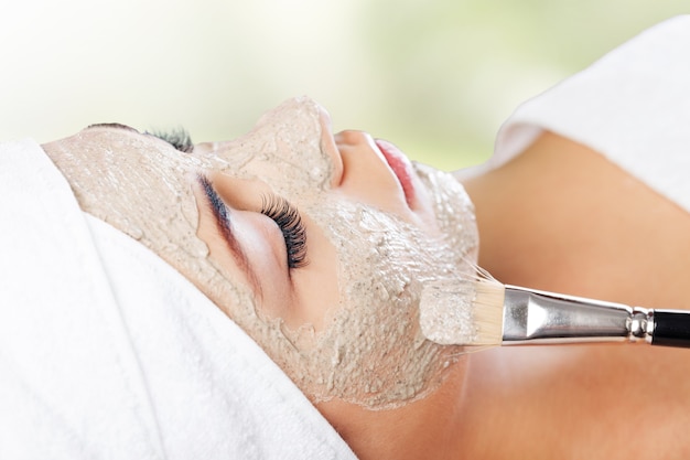 Attractive young woman applying healing mask on her face with brush