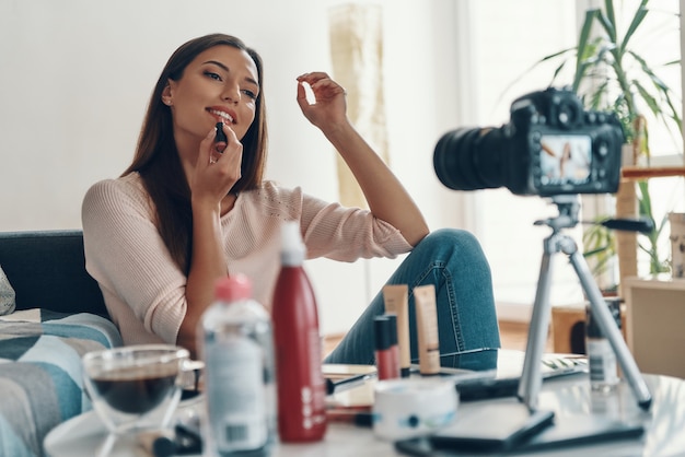 Attractive young woman applying lipstick and smiling while making social media video