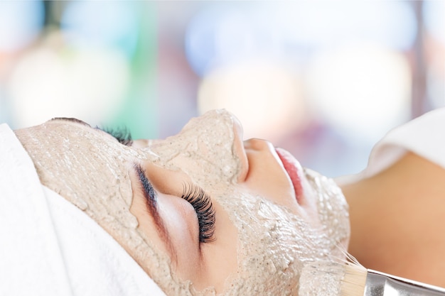 Attractive young woman applying mask on face with brush