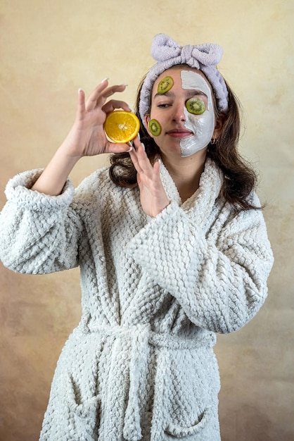 Attractive young woman applying white clay mask with fruit kiwi and orange