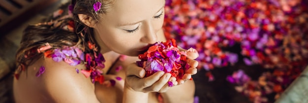 熱帯の花びらとアロマオイルスパトリートメントでお風呂にいる魅力的な若い女性