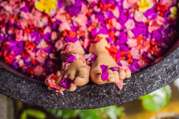 熱帯の花びらとアロマオイルスパトリートメントでお風呂にいる魅力的な若い女性