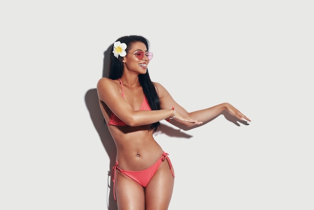 Attractive young woman in bikini dancing hula and smiling while standing against grey background