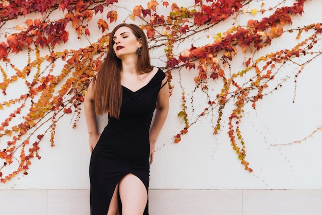 Attractive young woman in a black beautiful dress posing against an unusual wall background, eyes closed