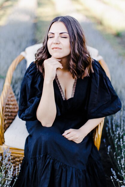 Attractive young woman in black dress and sitting in chair surrounded by lavender field