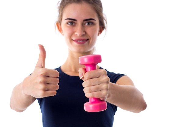 Photo attractive young woman in blue tshirt holding pink dumbbell and showing thumb up in studio