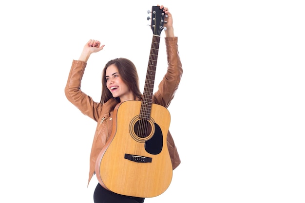 スタジオで白い背景の上のギターを保持している茶色のジャケットの魅力的な若い女性