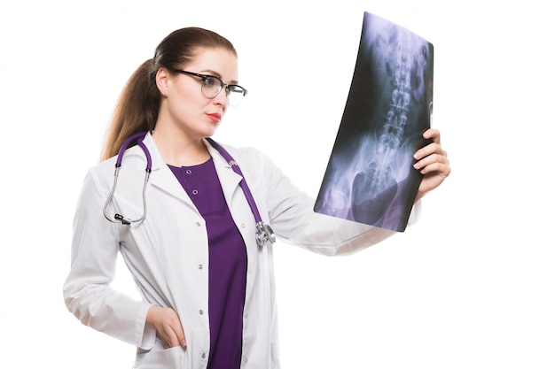 Attractive young woman doctor looking at x-ray making diagnosis in white uniform on white 