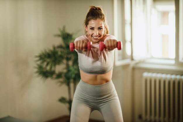 An attractive young woman doing exercises with dumbbell at home during the day.