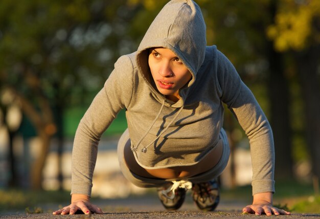 Привлекательная молодая женщина делает push ups на открытом воздухе