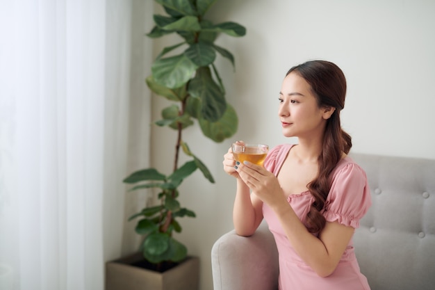 Attractive young woman drinking a cup of coffee while relaxing on a sofa at home