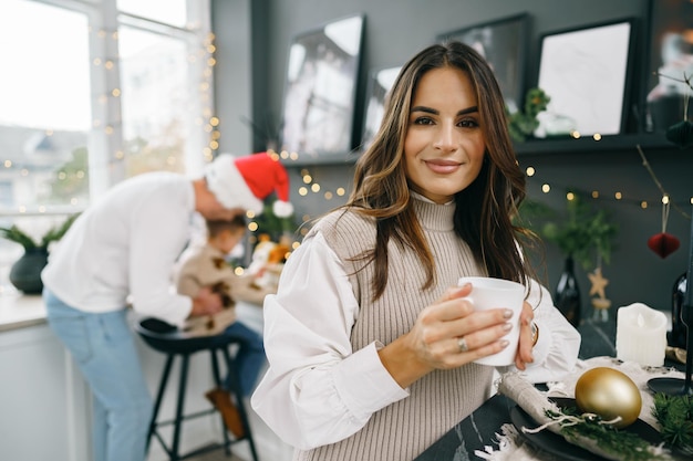 魅力的な若い女性はクリスマスのためにキッチンでお茶を飲みます