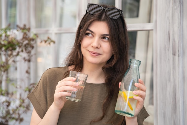 La giovane donna attraente beve l'acqua con il limone